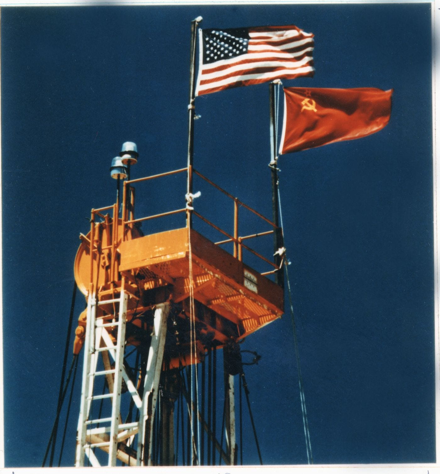 U.S. and Soviet flags fly side by side atop the experimental tower at the Nevada Test Site during the first of two Joint Verification Experiments. (Image via Lawrence Livermore National Laboratory.)